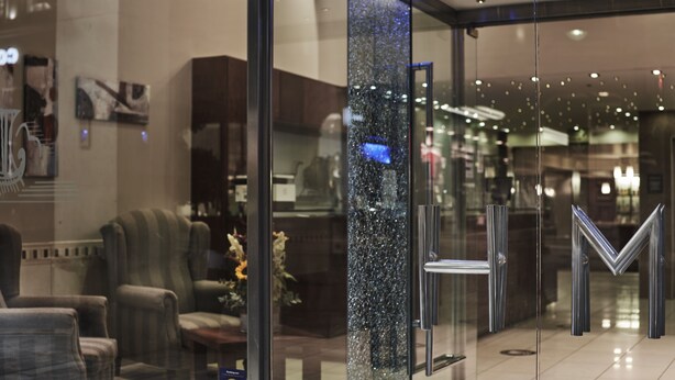 A hotel lobby with a reception desk, seating area, and a glass wall with a decorative element.