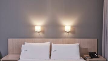 A hotel room with a wooden headboard, two bedside lamps, a telephone on the nightstand, and pillows labeled "Hotel Mediterranee".