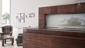 A reception area with a wooden desk, a chair, and a coffee table. There are framed artworks on the wall.