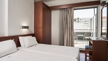Habitación de hotel con una cama grande, un escritorio y vistas a la ciudad a través del ventanal.