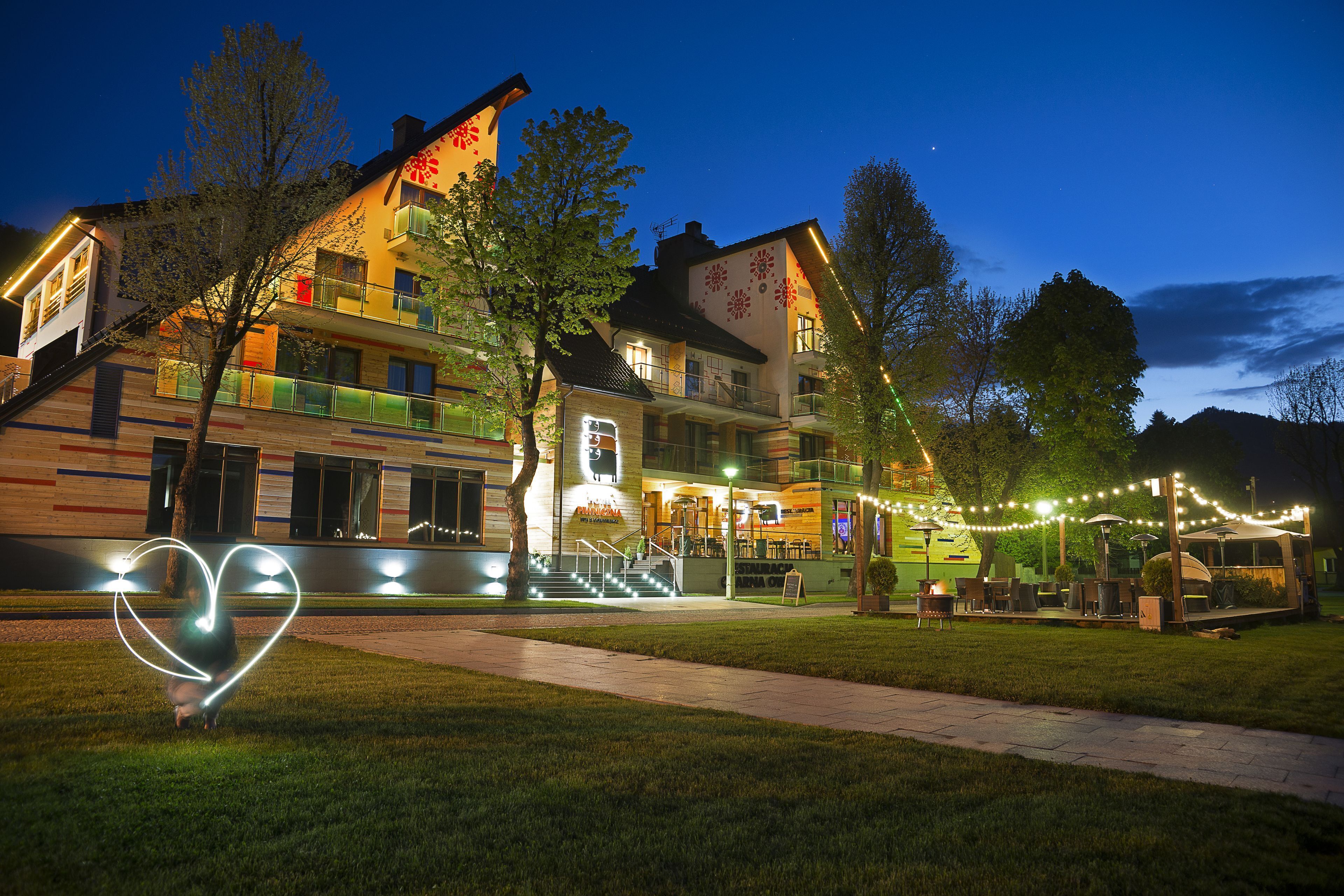 A multi-story building with a staircase leading to the entrance, outdoor seating, and string lights.