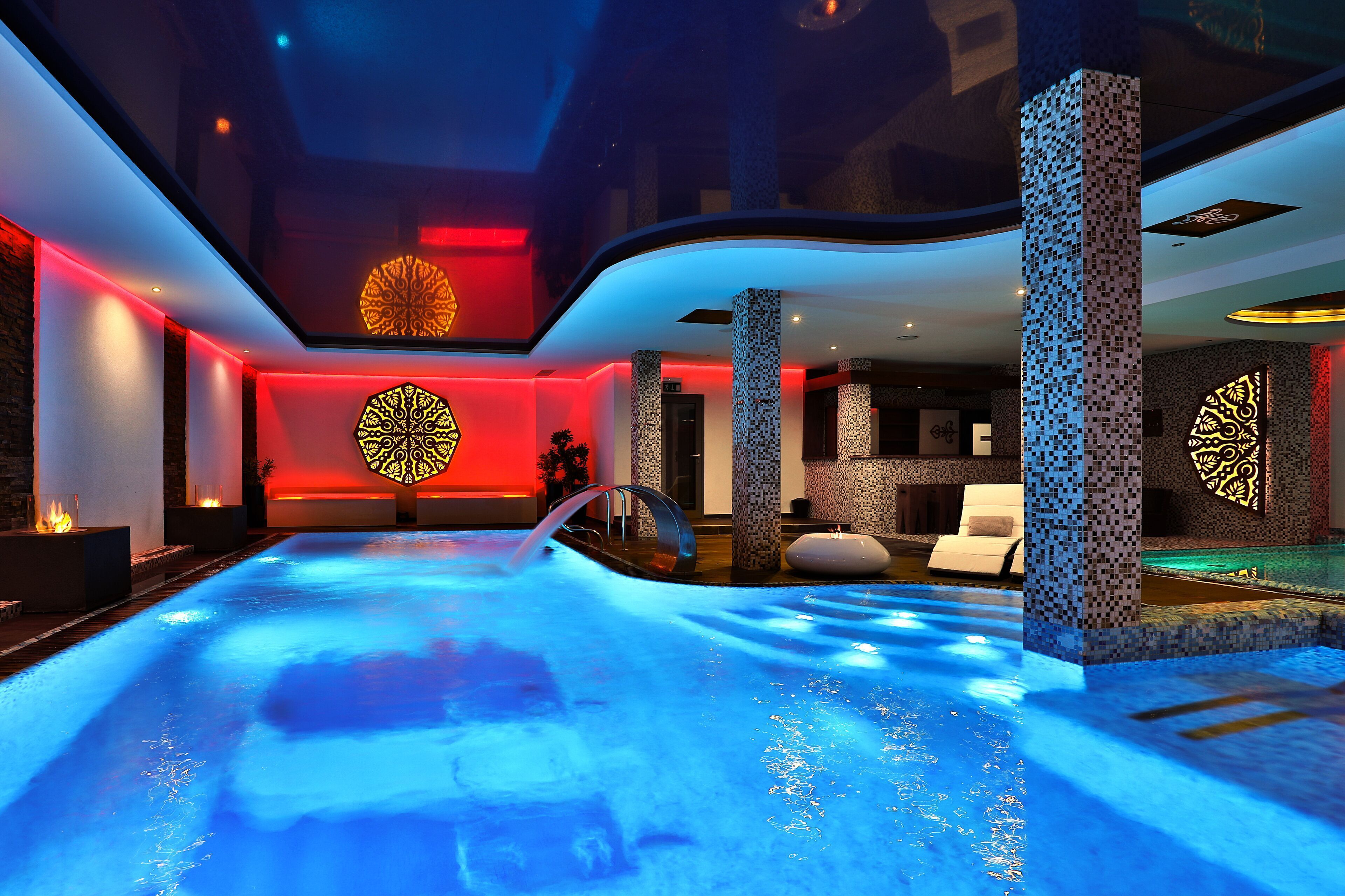 A modern indoor pool with a blue-lit water feature, surrounded by stone pillars and ambient lighting.