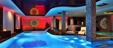 A modern indoor pool with a blue-lit water feature, surrounded by stone pillars and ambient lighting.