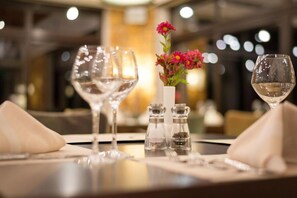 Una mesa de comedor dispuesta con copas de vino, un jarrón con flores y saleros y pimenteros.