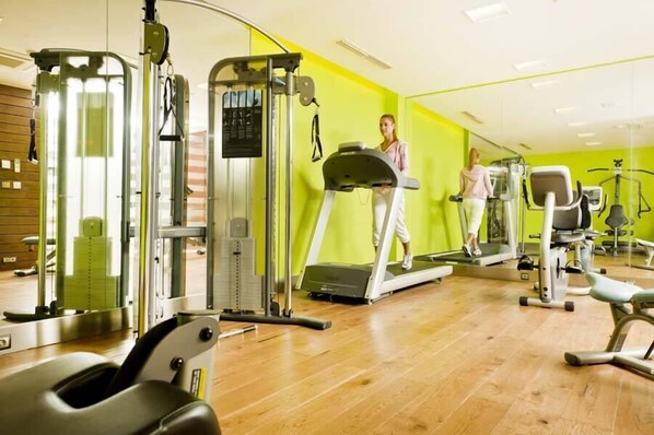 Un gimnasio con máquinas de cardio, equipo de entrenamiento de fuerza y un espejo grande.