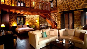 Cómoda habitación de hotel con pared de piedra, escalera de madera, cama, dos sofás y una mesa de centro.