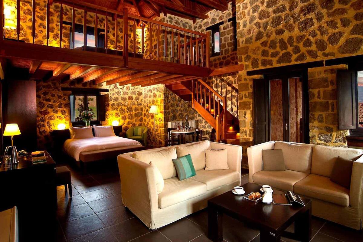A cozy hotel room with a stone wall, a wooden staircase, a bed, two sofas, and a coffee table.