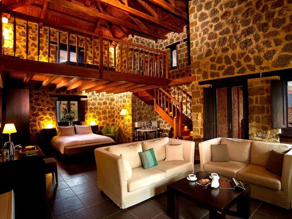 A cozy hotel room with a stone wall, a wooden staircase, a bed, two sofas, and a coffee table.