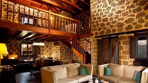 Amplia sala de estar con techo de madera alto, paredes de piedra y una chimenea acogedora. Hay dos sofás y una mesa de centro con aperitivos.