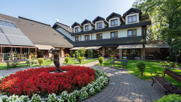A courtyard with a central flower bed, benches, and a building with multiple windows and a sloped roof. - Hotel Badura (Wadowice)
