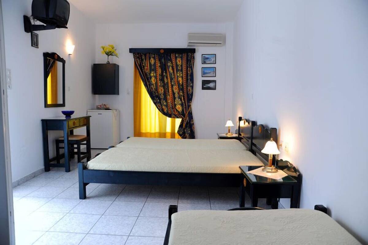 A hotel room with two beds, a desk, a chair, a TV, a lamp, and a window with curtains.