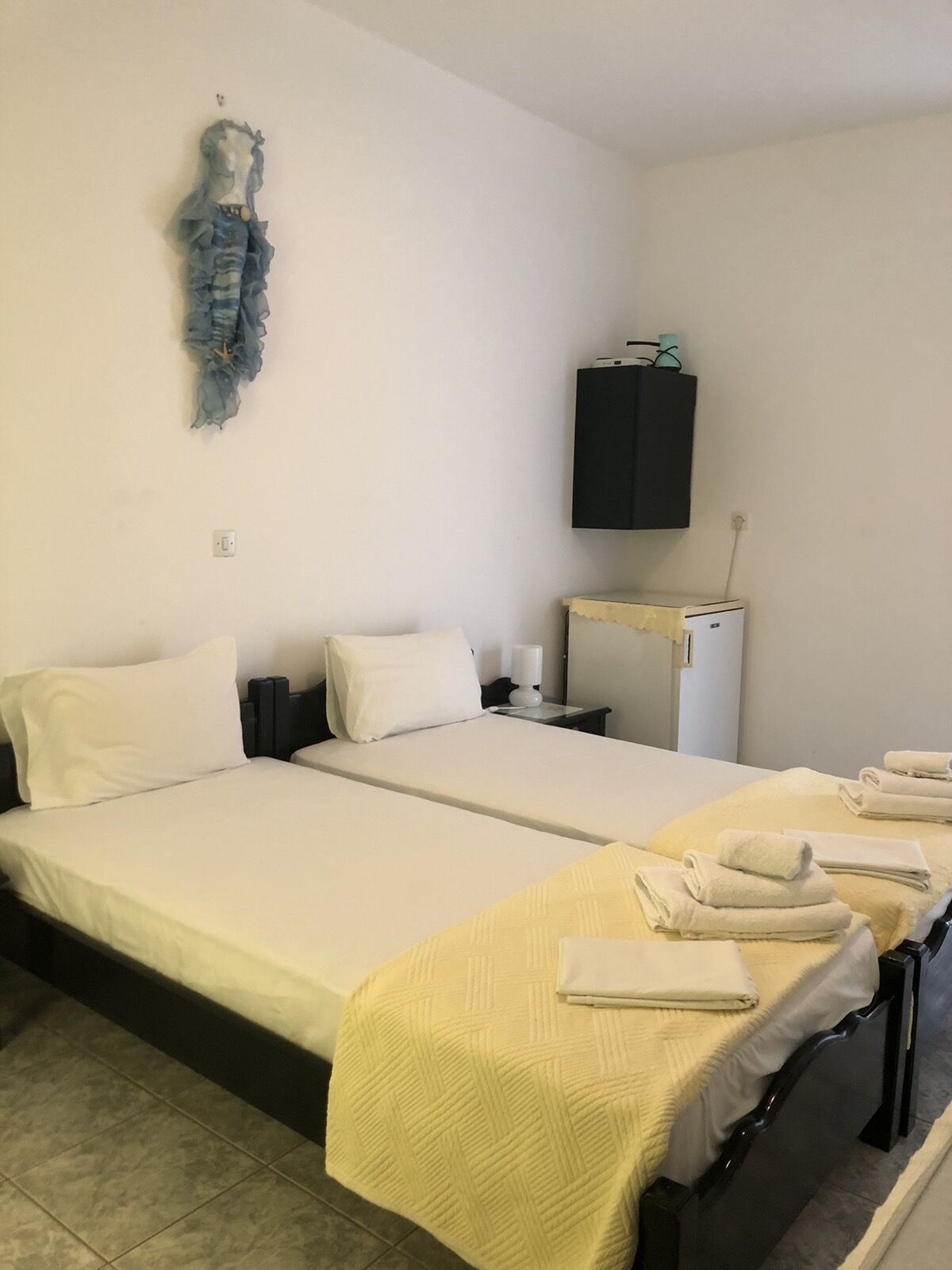 A hotel room with two beds, a small desk, a wardrobe, and a decorative item on the wall.
