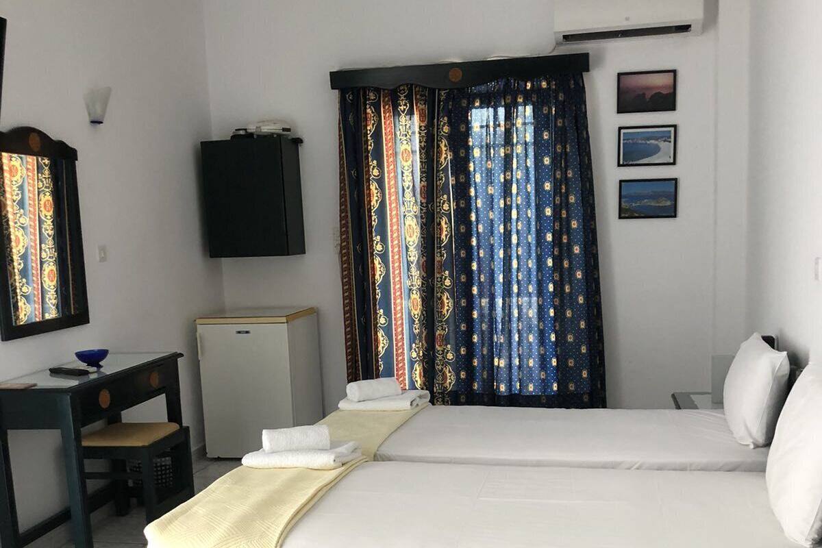 A hotel room with a bed, a desk, a chair, a TV, and a window with patterned curtains.