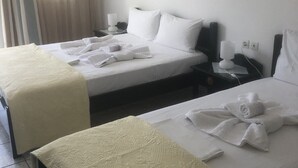 A hotel room with two beds, each with white linens and towels, a bedside table with a lamp, and a wall-mounted air conditioner. - Atlantis Place Milos (Milos)