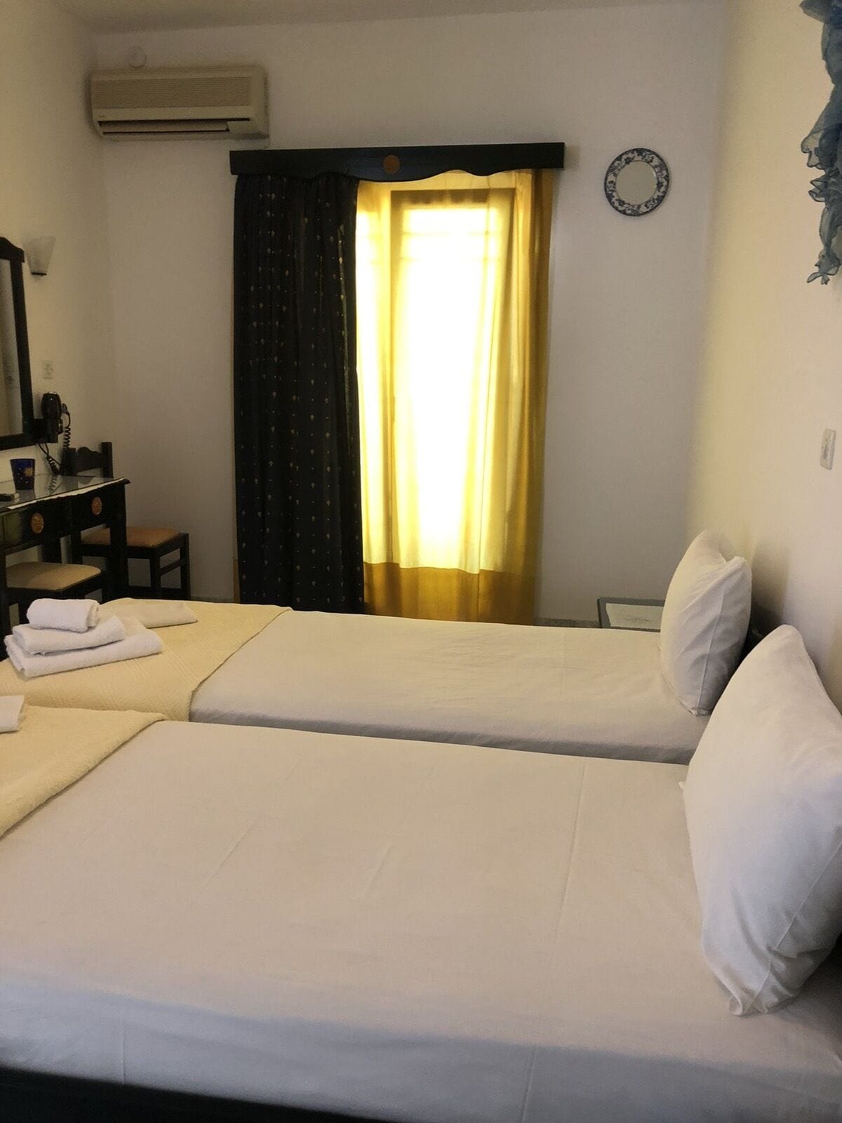 A hotel room with two single beds, a desk with a telephone, and a window with curtains.