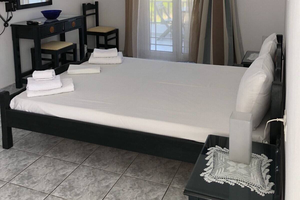 A hotel room with a bed, a desk with a chair, a small table with a lamp, a mirror, and a window with curtains.