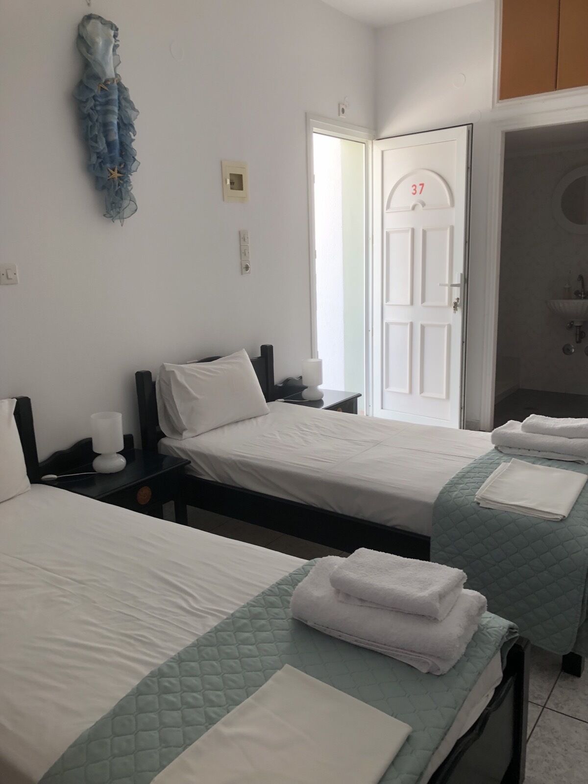 Habitación de hotel con dos camas, baño visible a través de una puerta abierta y un perchero con toallas.