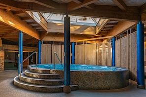 A multi-tiered hot tub with a skylight above, surrounded by wooden walls and blue pillars. - Hotel Die Post (Bad Kleinkirchheim)