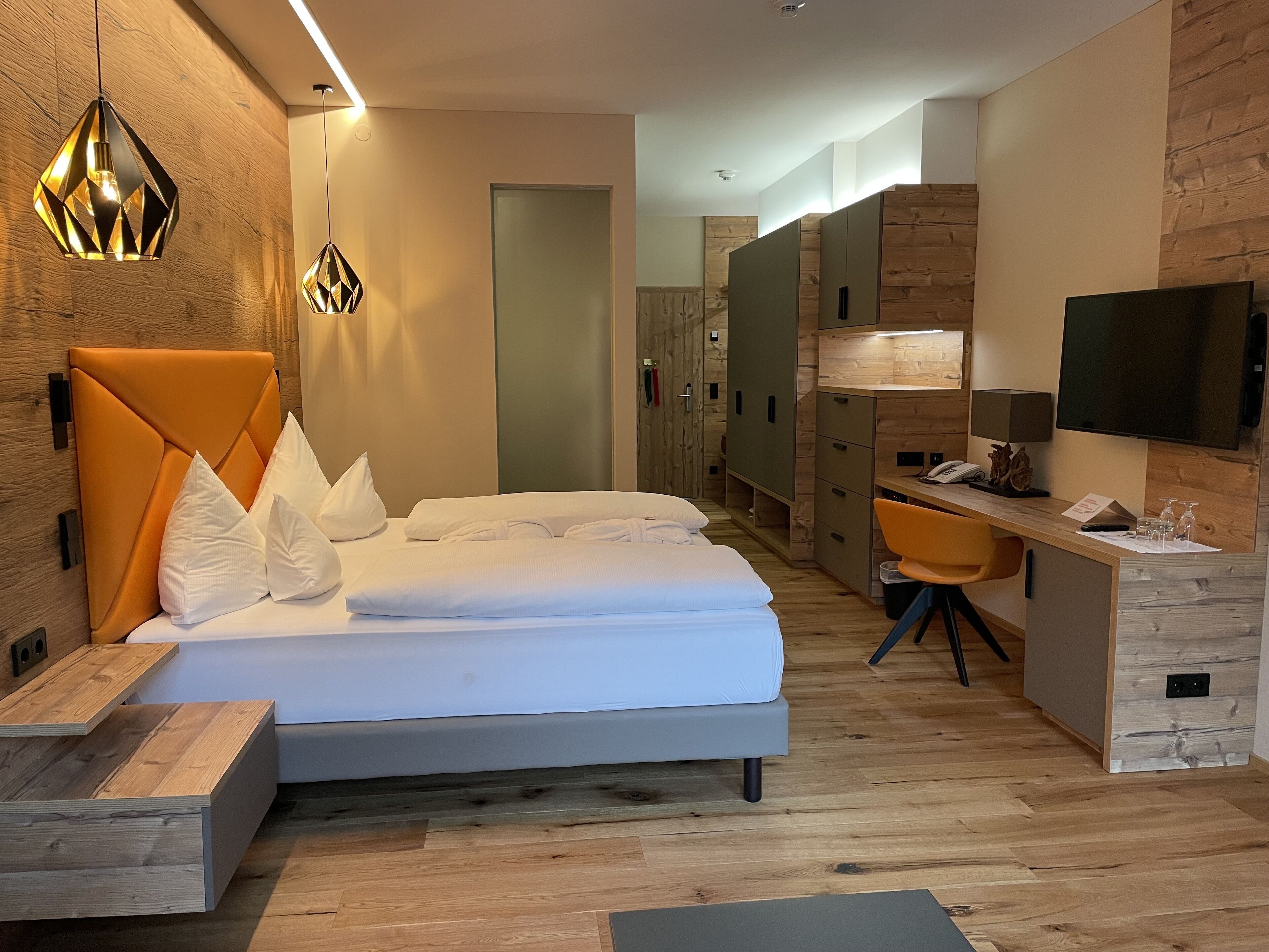 Una habitación de hotel moderna con cama, escritorio, silla, televisor y armario.