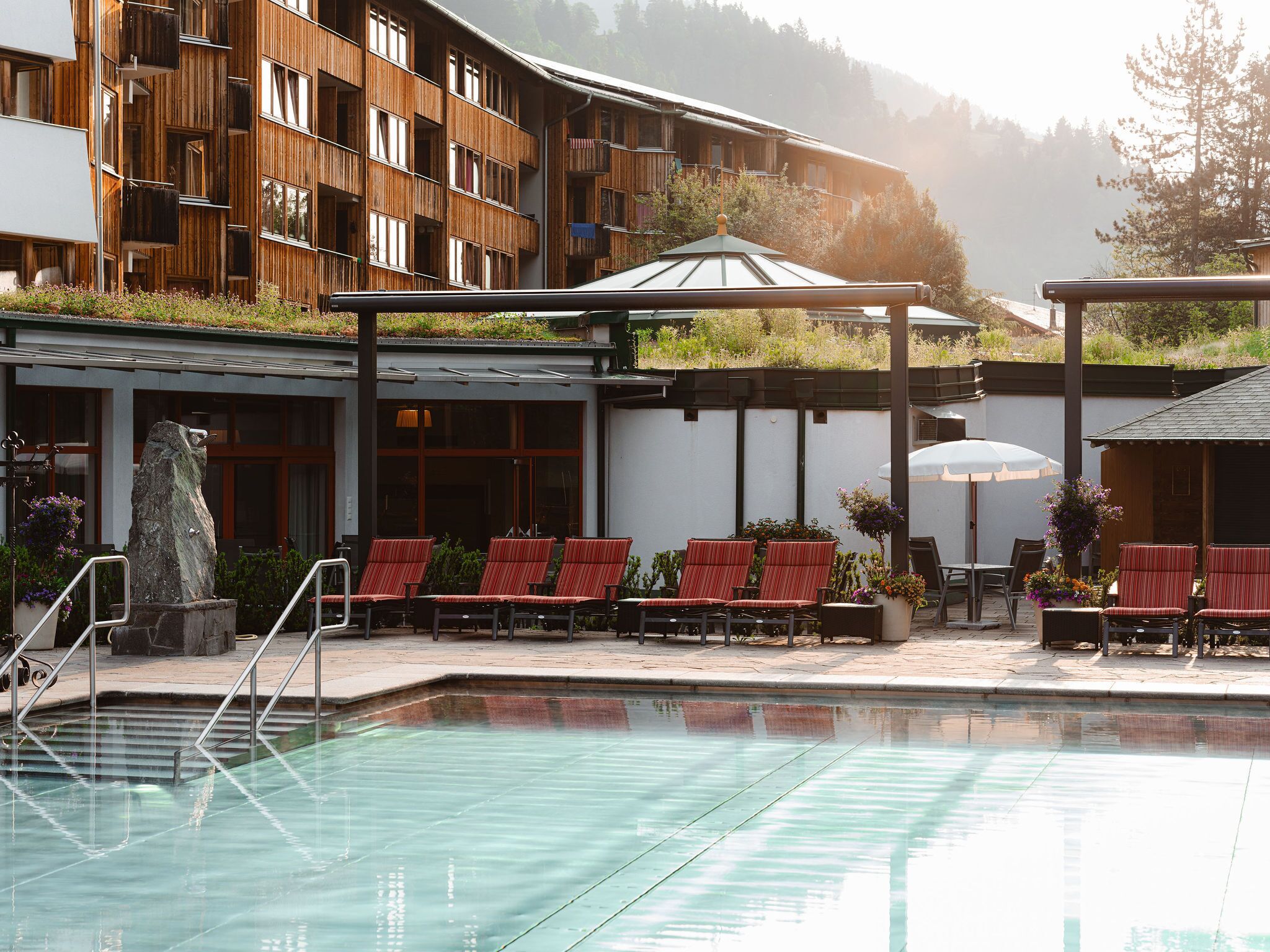 Un área de piscina con sillas de descanso, una escultura de piedra y un edificio con balcones de madera.
