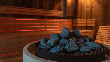 A sauna with a circular seating area filled with rocks, wooden benches, and red ambient lighting.