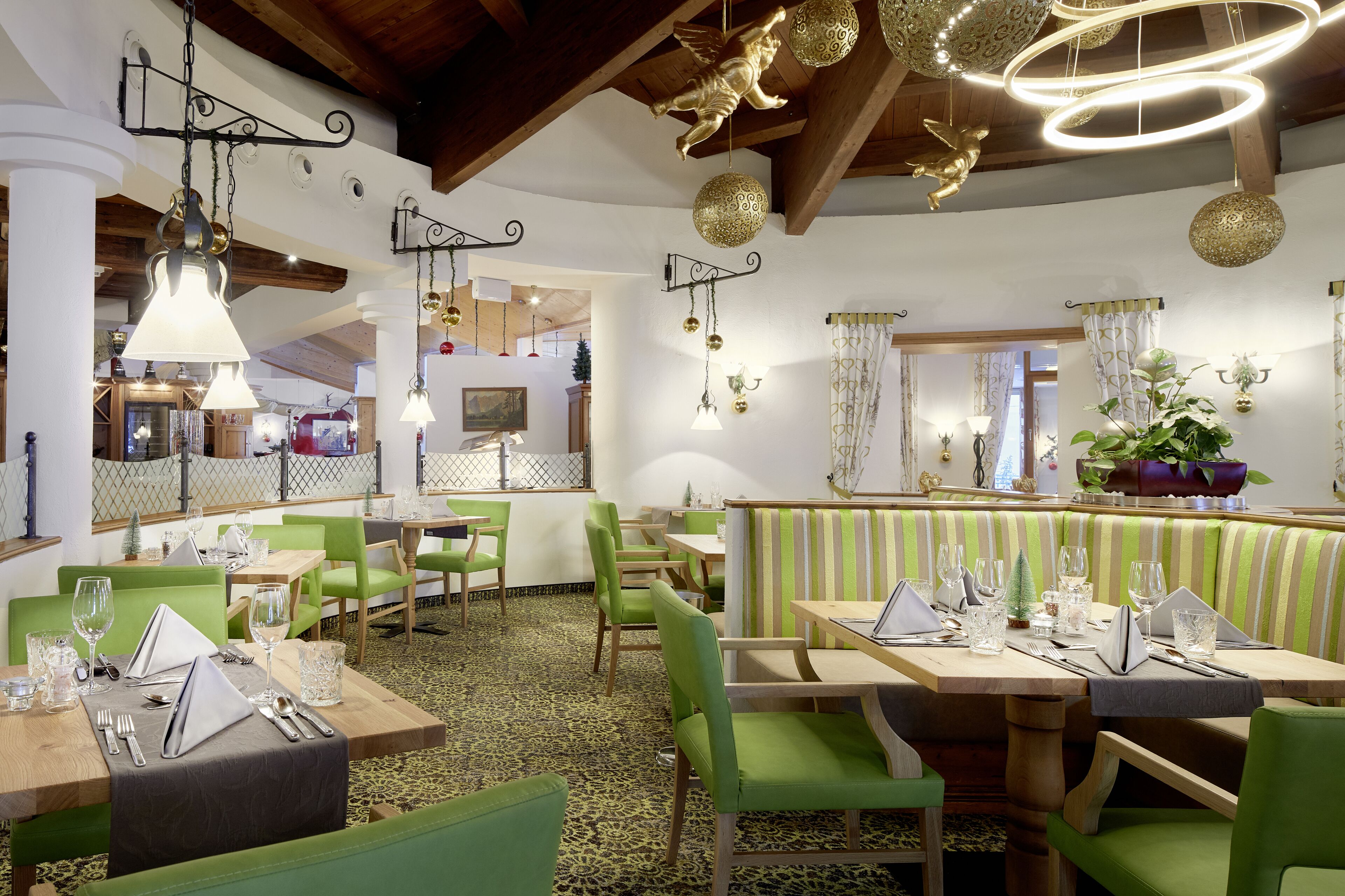 Un restaurant avec des sièges recouverts d’un tissu vert, des tables en bois et des luminaires décoratifs suspendus.
