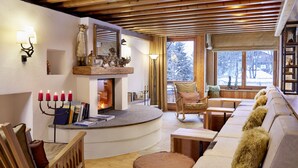 Una sala acogedora con chimenea, muebles de madera y vistas del paisaje nevado.