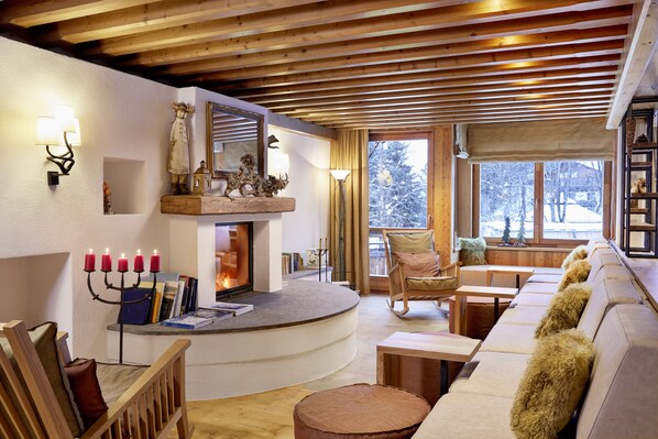A cozy living room with a fireplace, wooden furniture, and a view of the snowy outdoors.