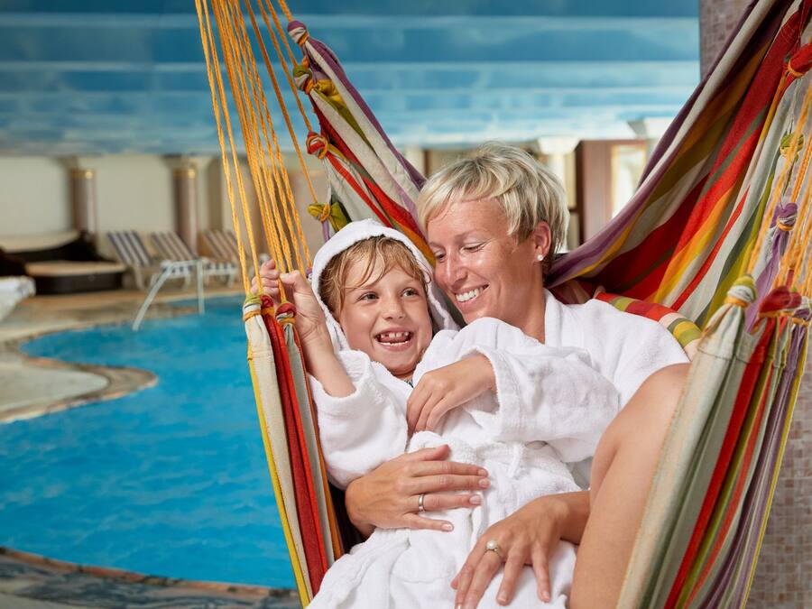 Ett par ligger i en hängmatta vid en pool, med solstolar och ett område vid poolkanten i bakgrunden.