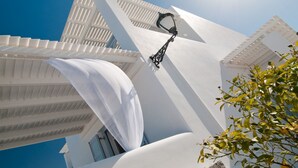 A white building with a modern design, featuring a prominent white awning and a black outdoor light fixture. - Miland Suites (Milos)