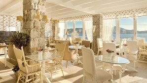 A spacious dining area with high ceilings, stone walls, and large windows offering a view of the sea. - Miland Suites (Milos)