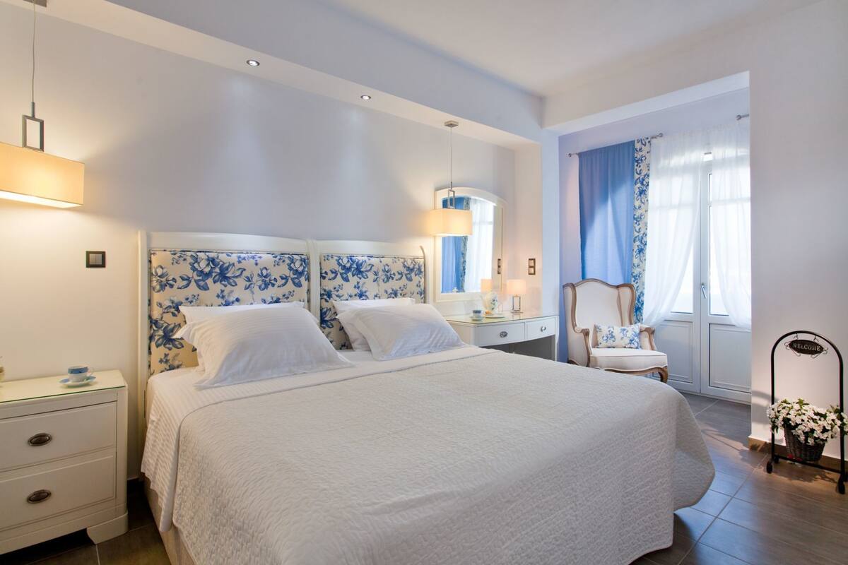 Habitación de hotel con una cama grande, una mesita de noche, una silla, una ventana con cortinas y un cartel de bienvenida.