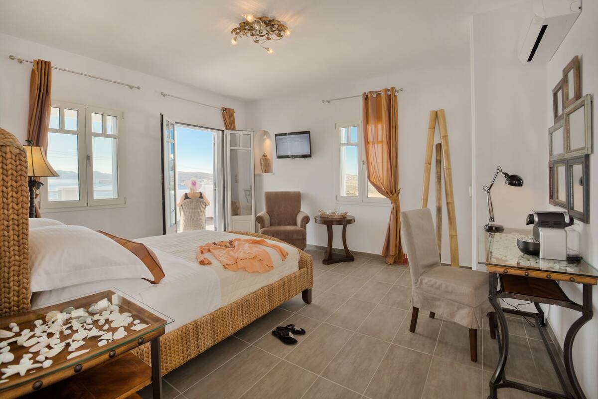 Habitación de hotel con cama, escritorio, silla, televisor y vistas al exterior.