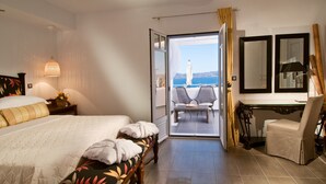 A hotel room with a bed, a sitting area with chairs, a table, and a view of the sea. - Miland Suites (Milos)
