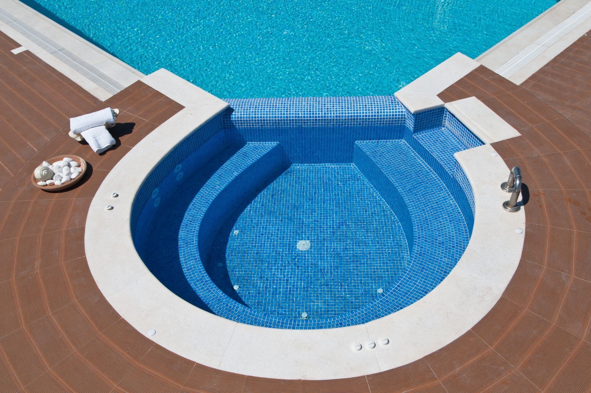 A circular hot tub with blue mosaic tiles, surrounded by a tiled deck.