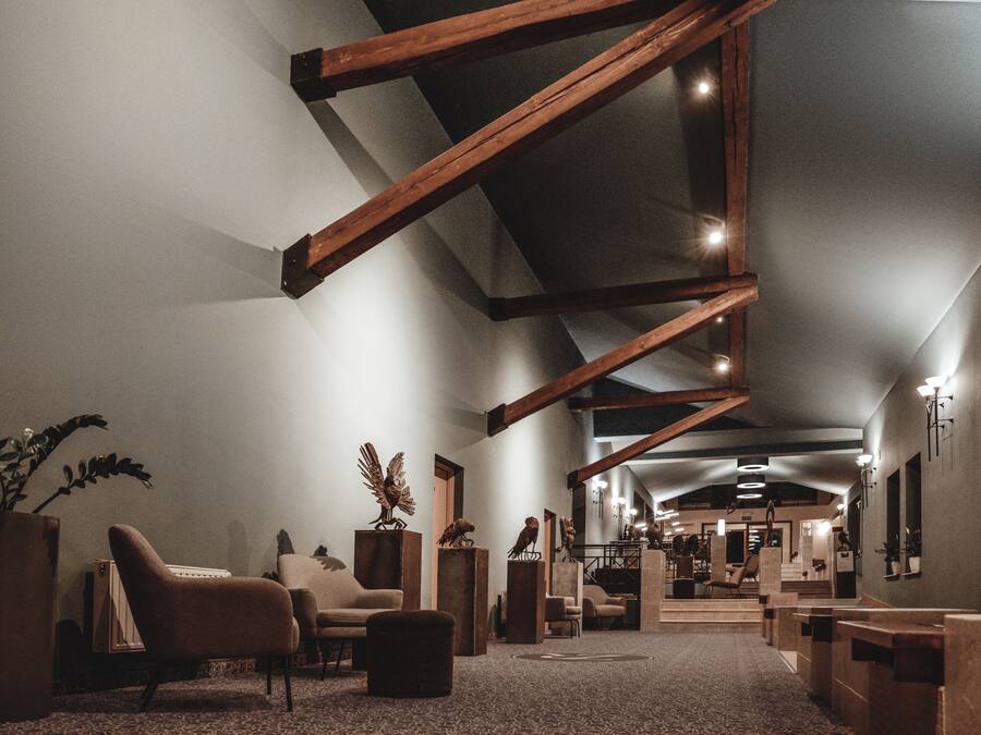 Ruime inrichting met hoge plafonds, houten balken en een centraal zithoek met banken en een salontafel.