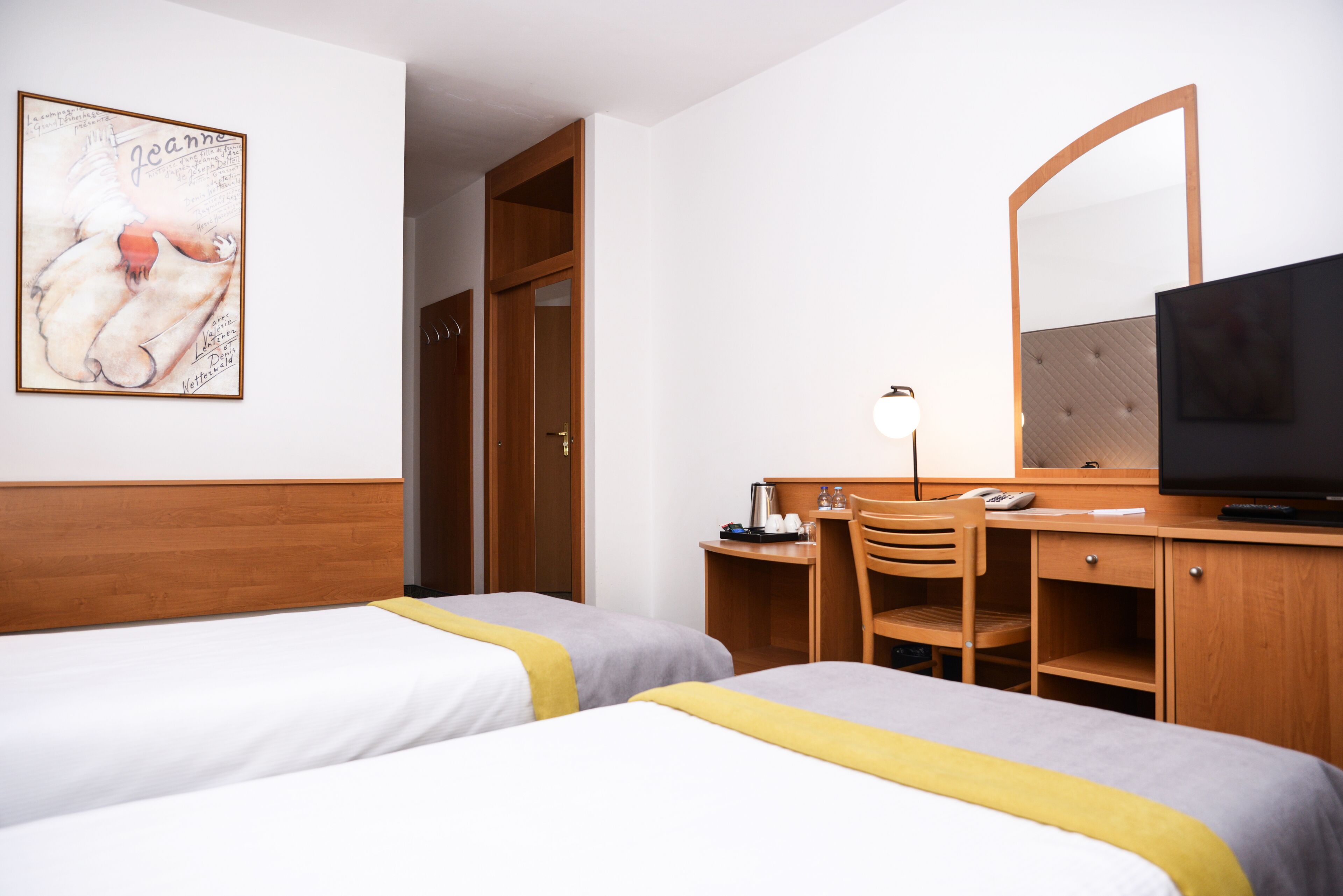 A hotel room with two beds, a desk with a chair, a television, a mirror, and a painting on the wall.