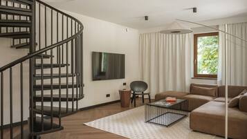 Una sala de estar moderna con una escalera de caracol, un televisor de pantalla plana, un sofá, una mesa de centro y un ventanal con cortinas.