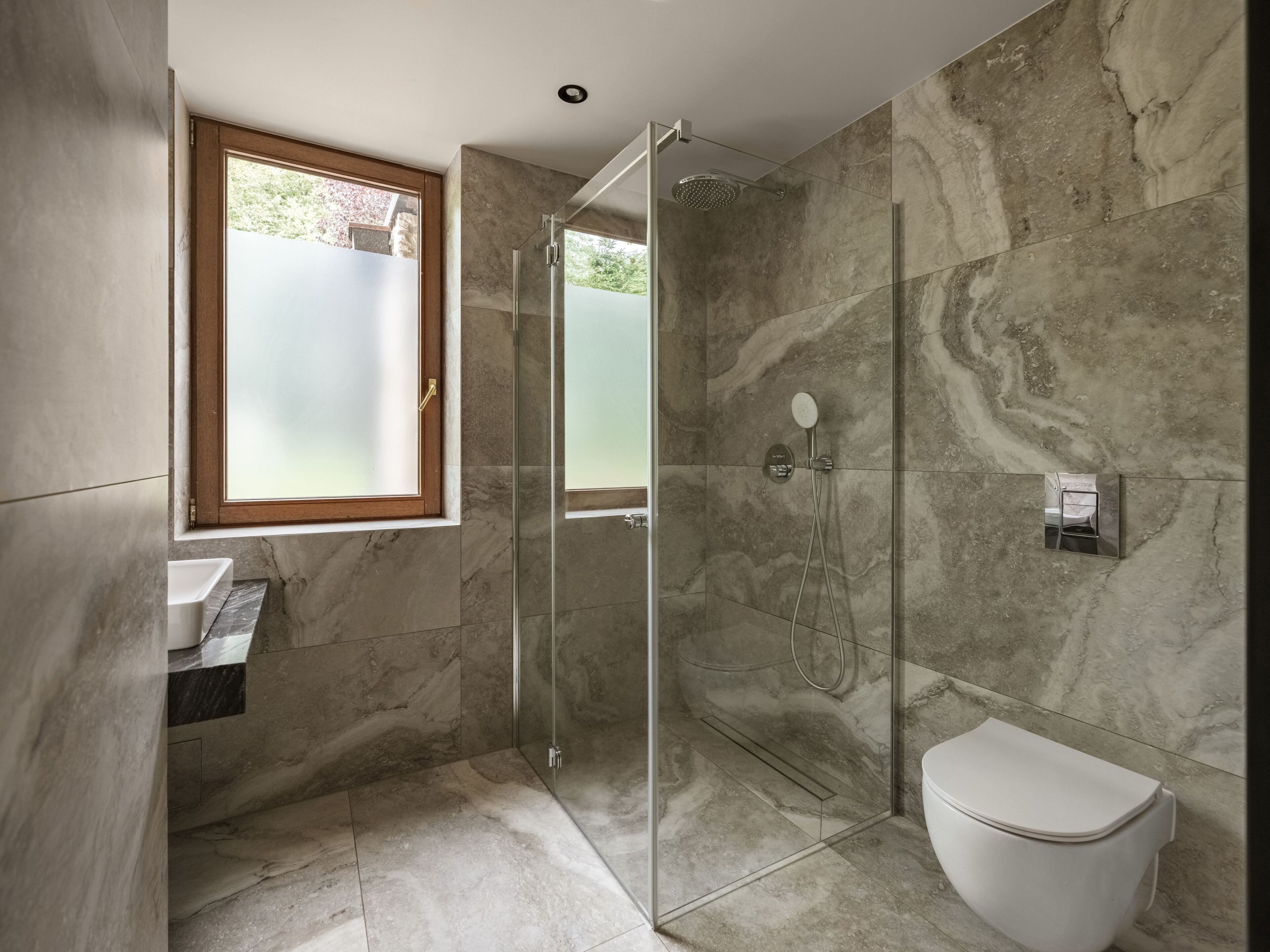A modern bathroom with a glass-enclosed shower, a toilet, and a window.