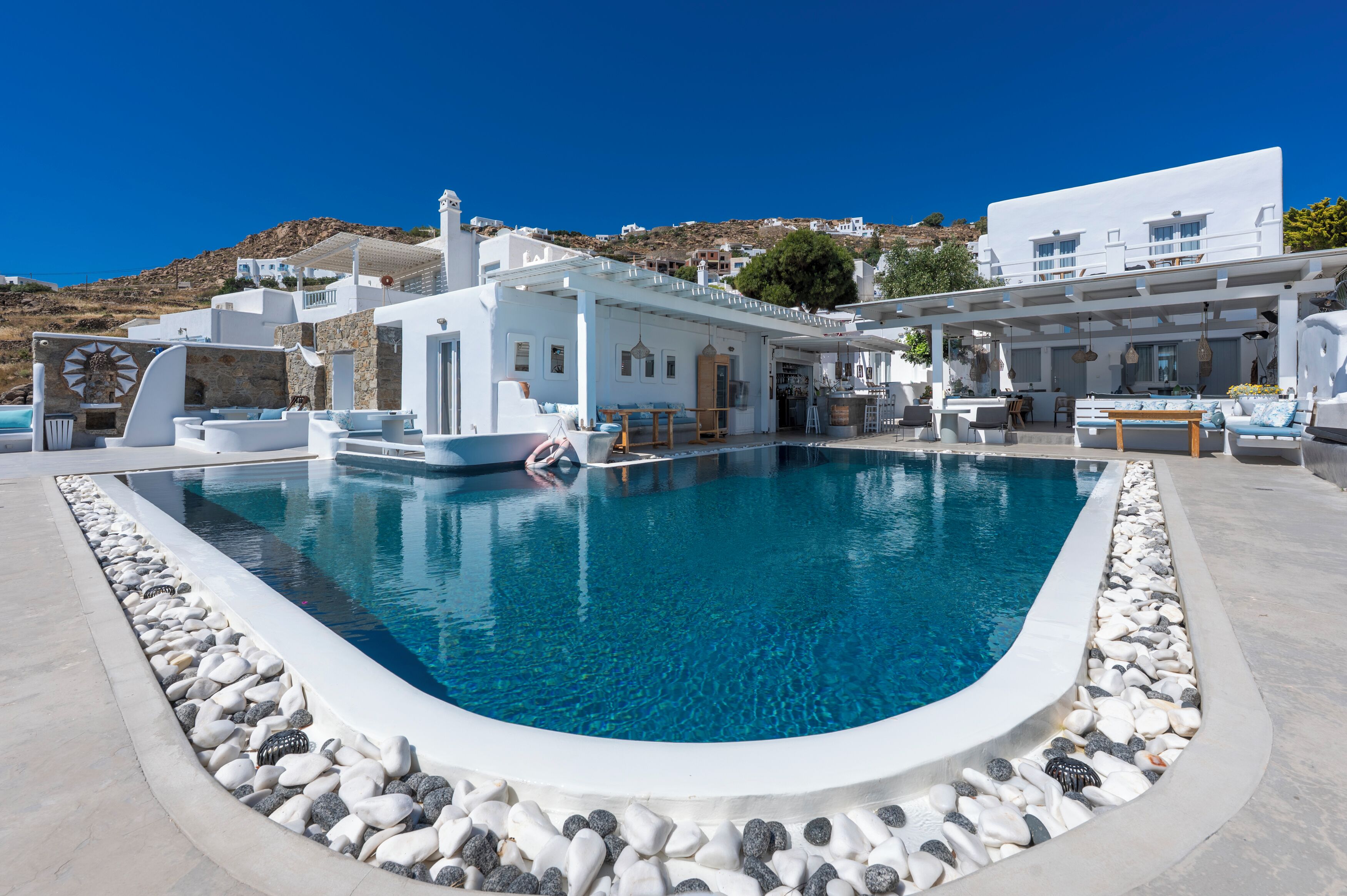 A pool area with a stone border, white buildings, and a clear blue sky.