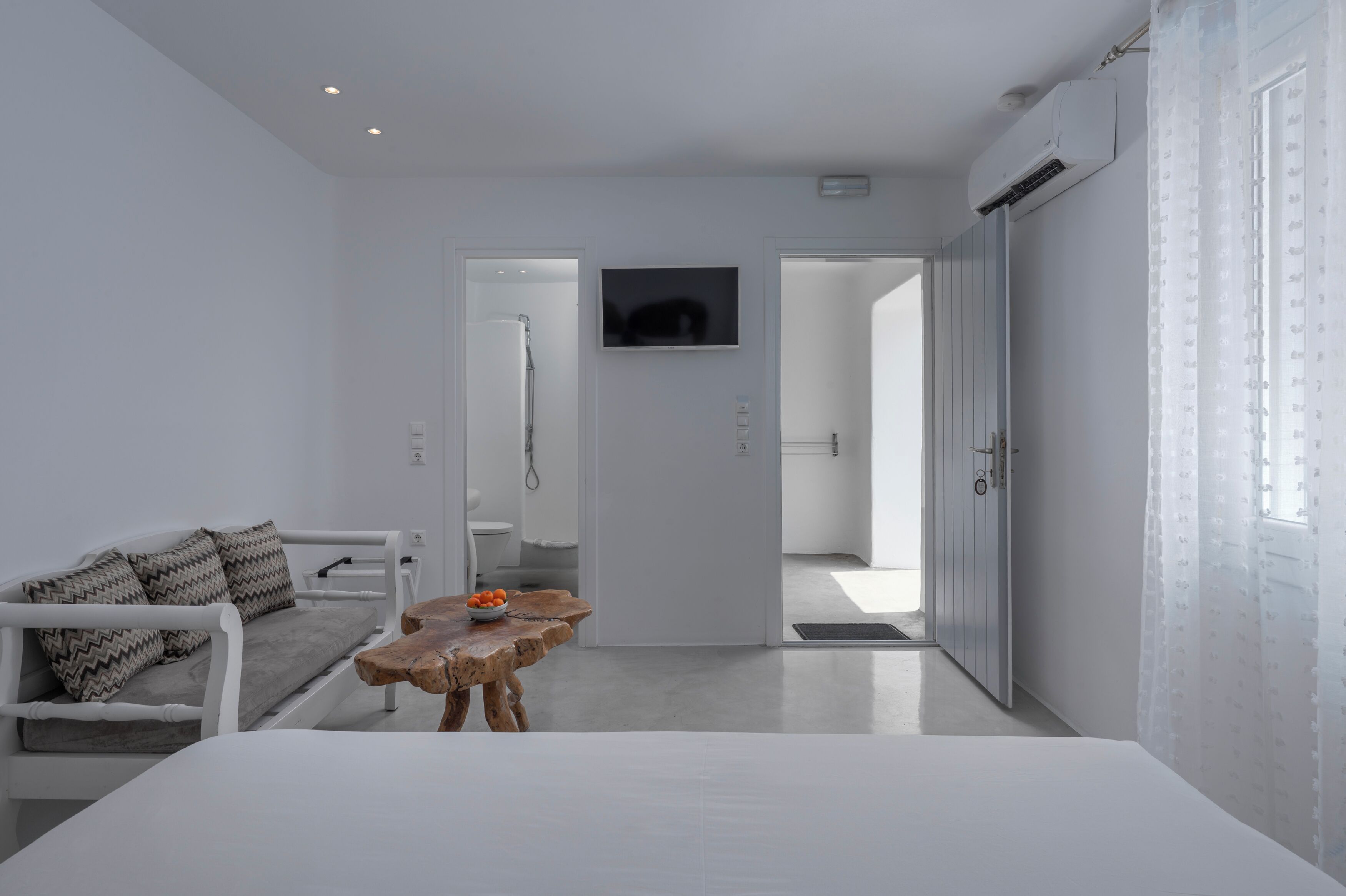 Una habitación moderna y minimalista con un sofá blanco, una mesa de madera con fruta y un televisor en la pared.
