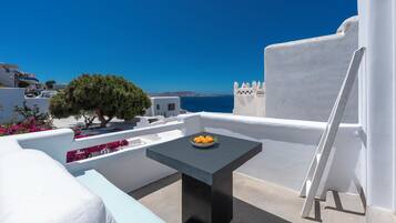 Una terraza de paredes blancas con una mesa, sillas, un árbol y vista al mar.