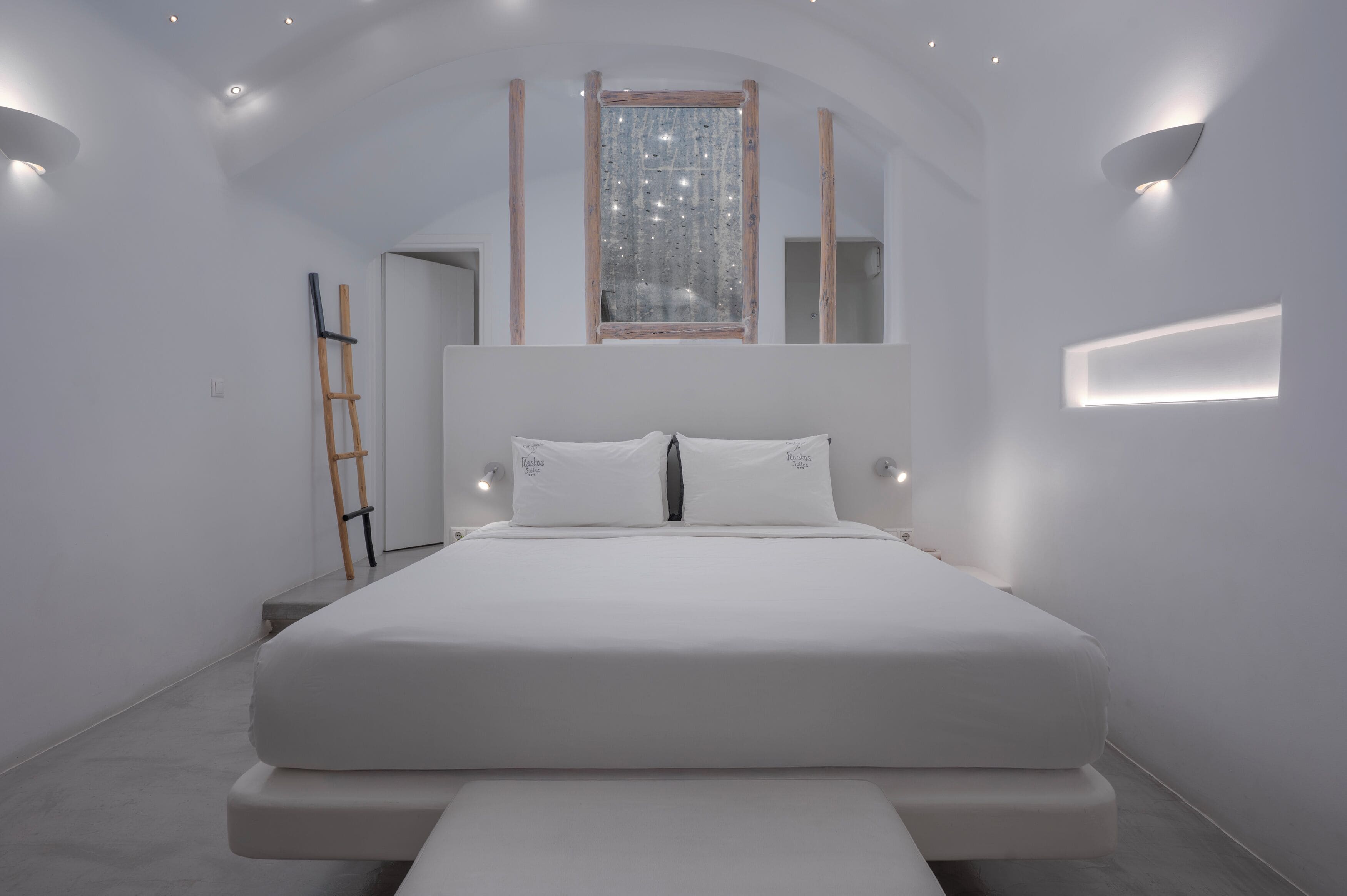A minimalist bedroom with a large bed, a ladder, and a window with a decorative frame.