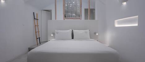 A minimalist bedroom with a large bed, a ladder, and a window with a decorative frame.
