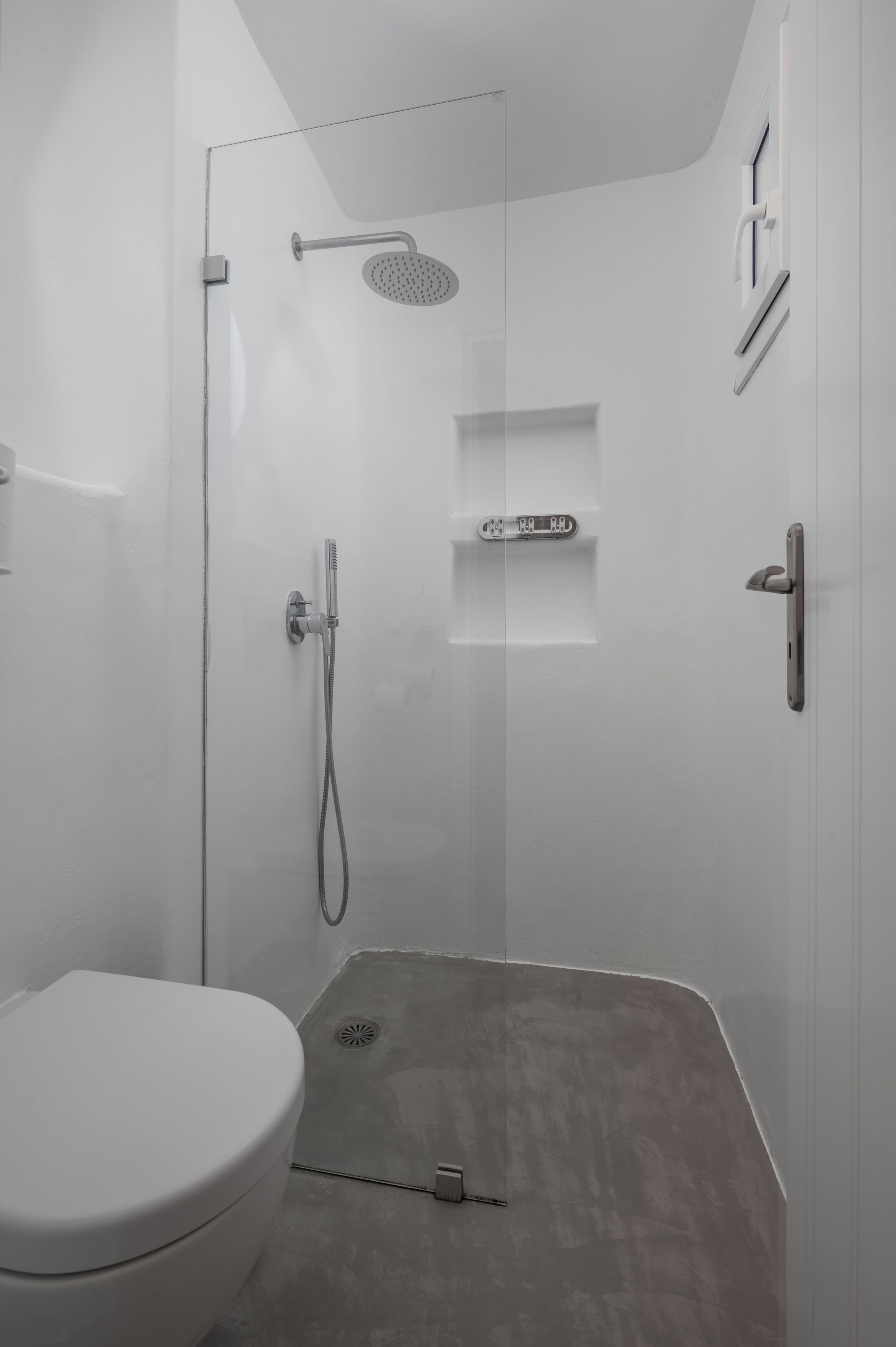 Un baño moderno con ducha, inodoro y un pequeño mueble con estantes.