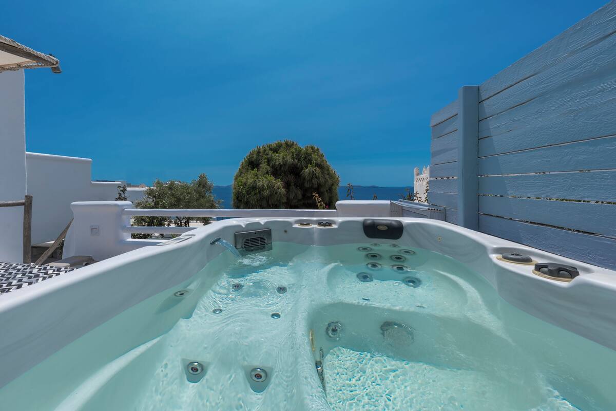 A hot tub with a clear view of the sea and a tree in the background.