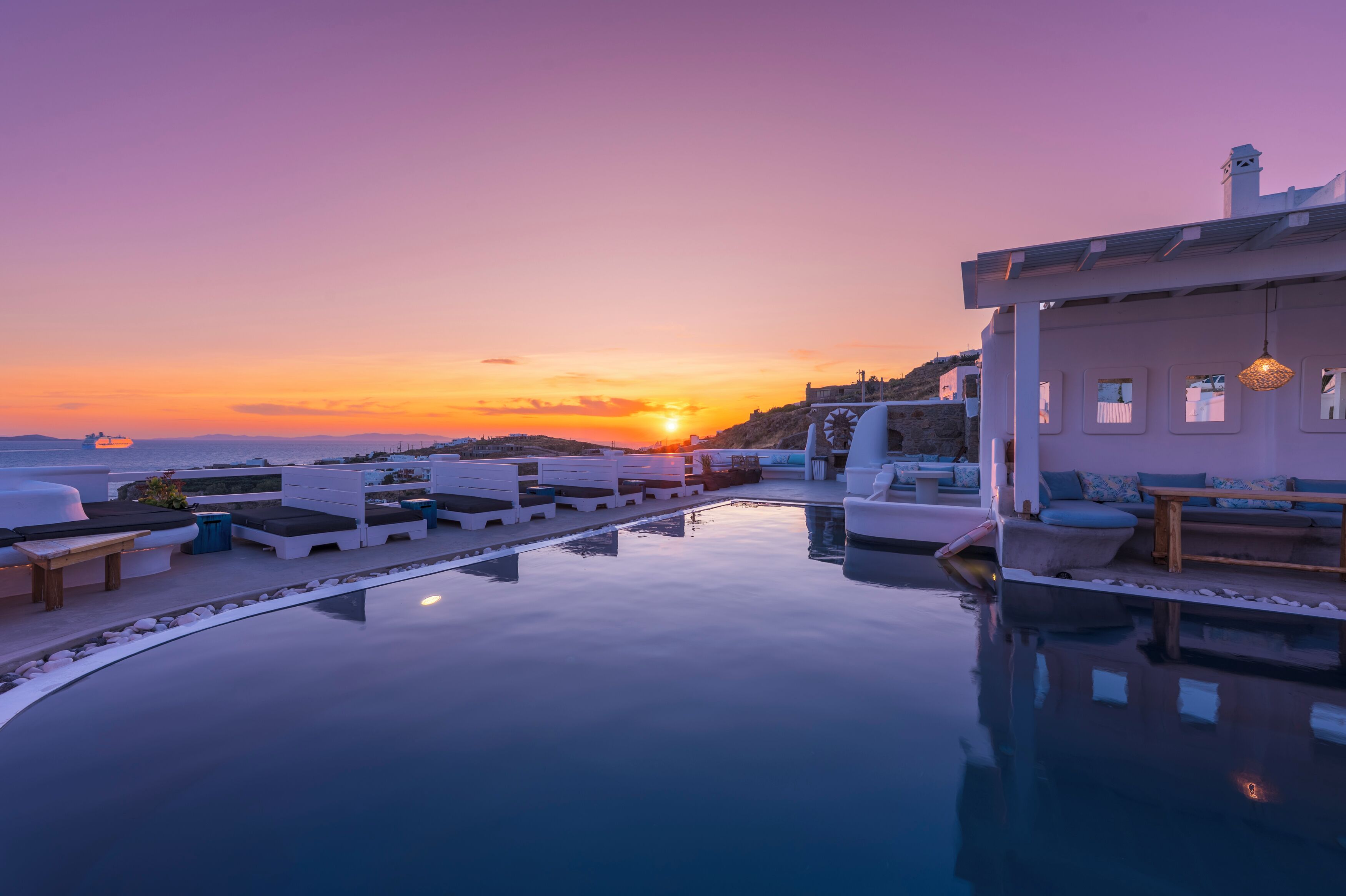 Un espace aménagé au bord de la piscine, avec des chaises longues et une vue sur le coucher de soleil sur la mer.