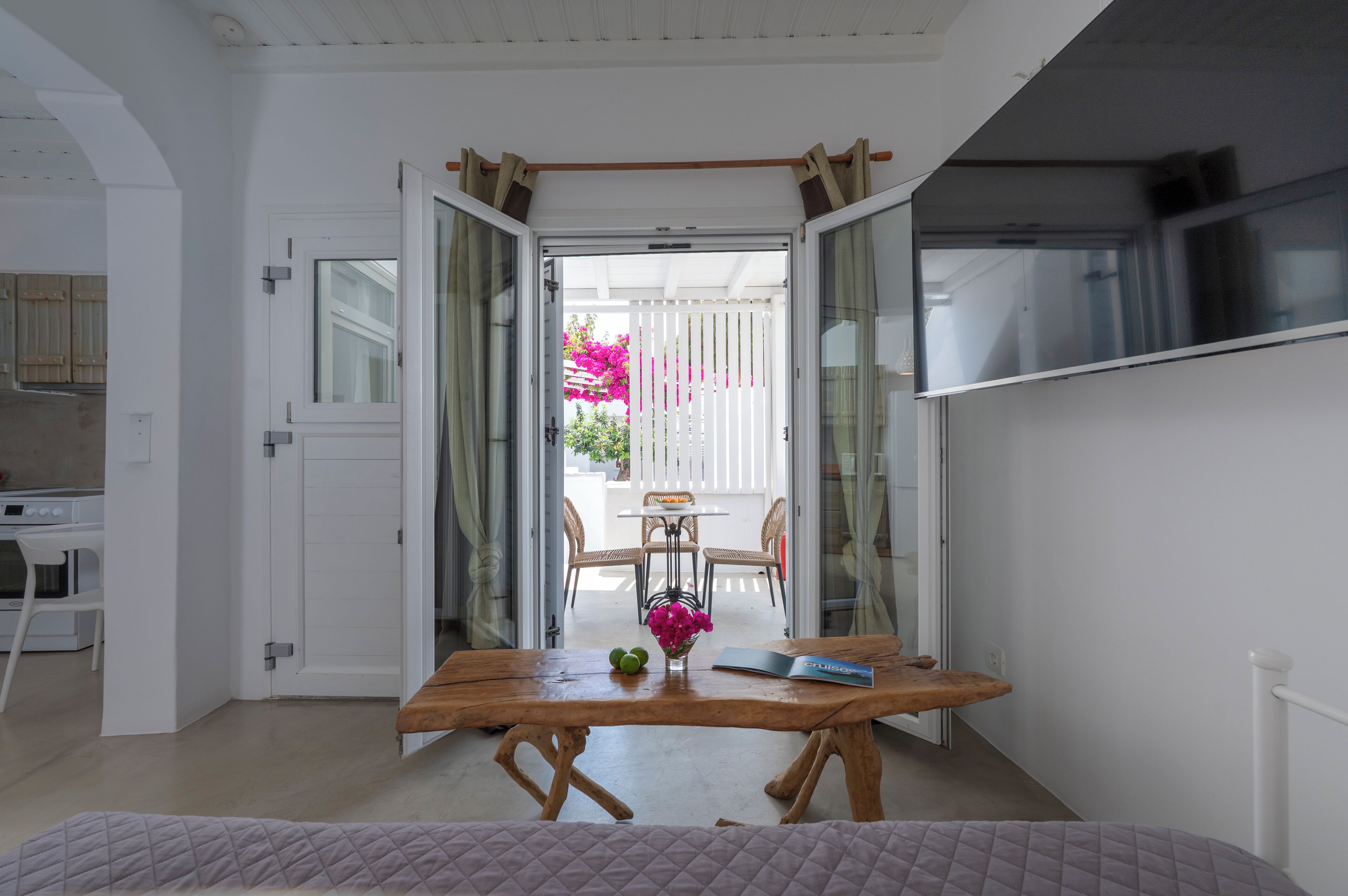 A room with a wooden table, a bed, and a view of an outdoor patio with chairs and a table.