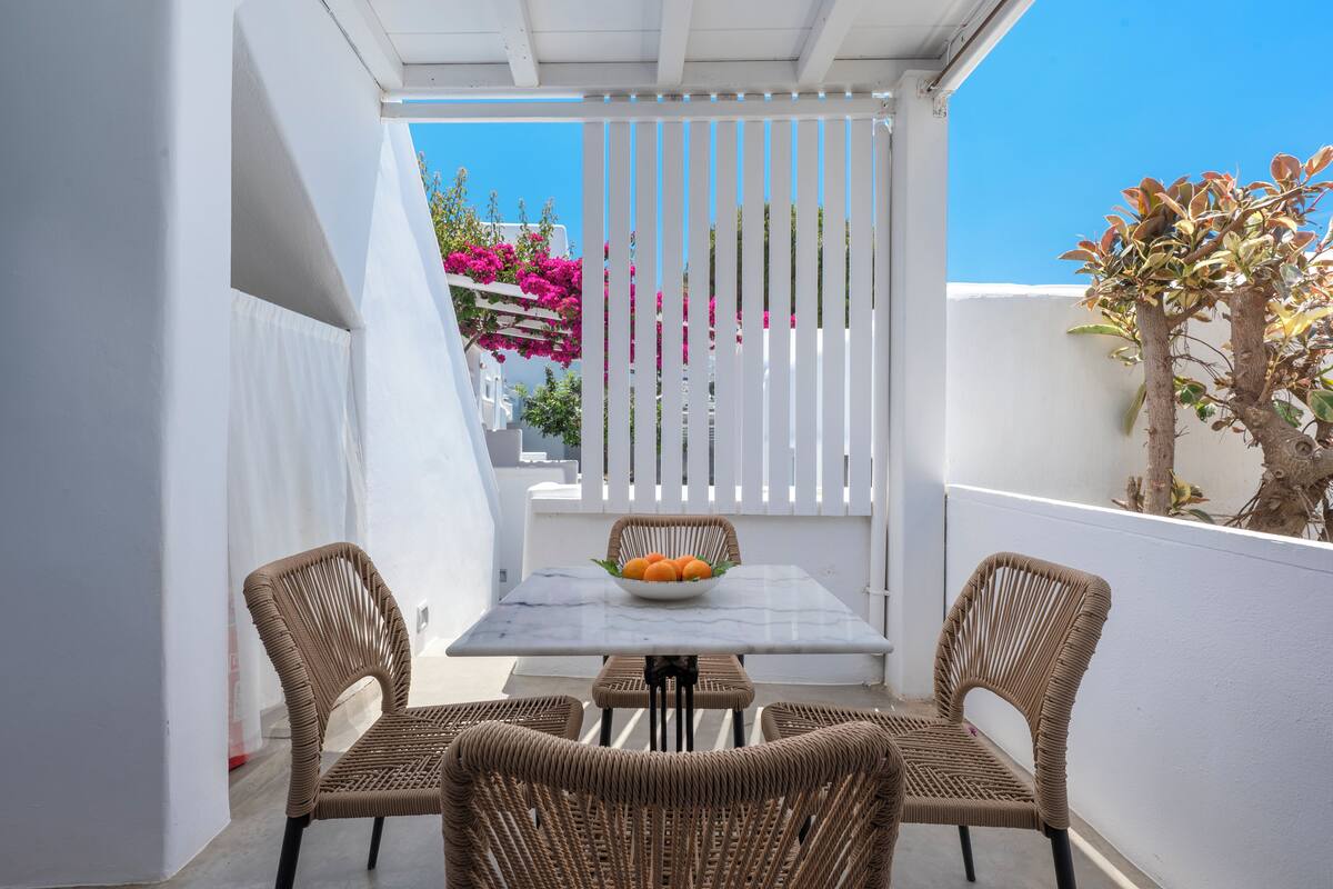 A white outdoor patio with a marble table, wicker chairs, and a bowl of fruit.