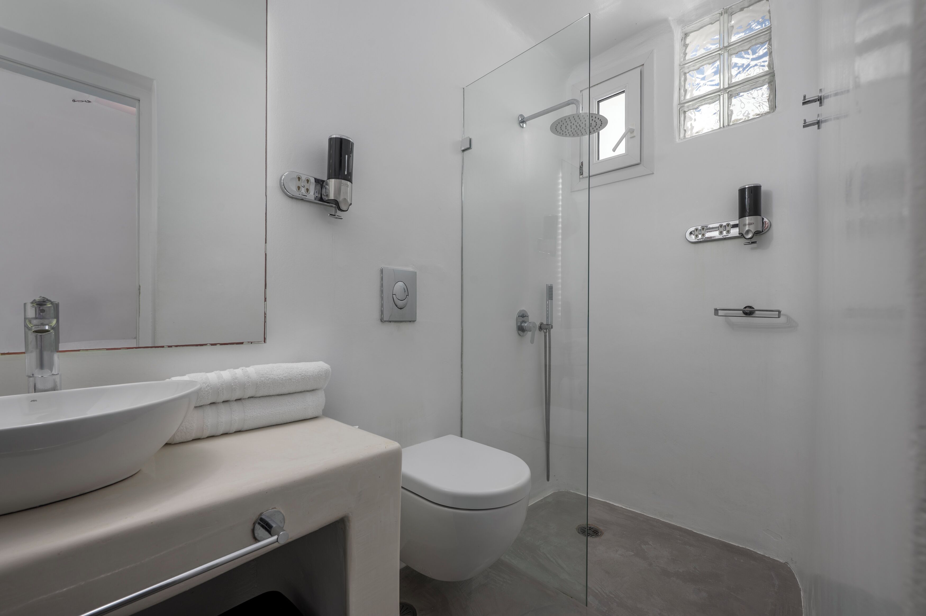 Un baño moderno con ducha de vidrio, un lavabo blanco y un inodoro.